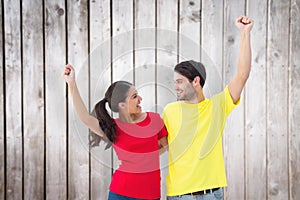 Composite image of excited couple cheering in red and yellow tshirts