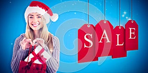 Composite image of festive blonde holding christmas gift and bag