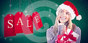 Composite image of festive blonde holding christmas gift and bag