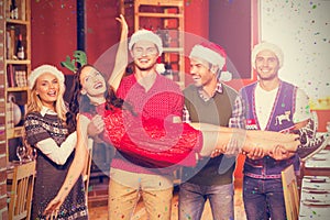 Composite image of friends with christmas hats carrying woman