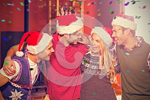 Composite image of friends wearing christmas hats looking at each other