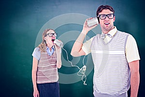 Composite image of geeky hipster couple speaking with tin can phone