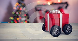 Composite image of gift box wrapped in red paper with ribbon on wheels