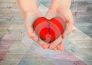 Composite image of hands holding broken heart against wood background