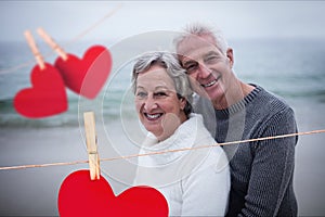 Composite image of hanging hearts and senior couple embracing on beach