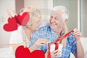 Composite image of hanging hearts and senior couple opening a gift box