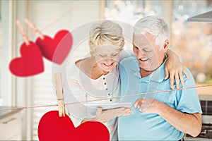 Composite image of hanging hearts and senior couple using digital tablet