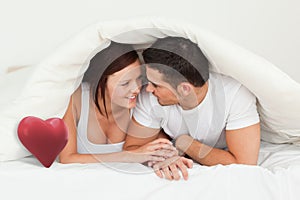 Composite image of happy couple hiding under a blanket