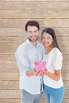 Composite image of happy couple showing their piggy bank