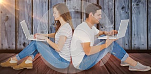 Composite image of happy couple sitting on floor back to back using laptop