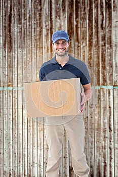 Composite image of happy delivery man holding cardboard box