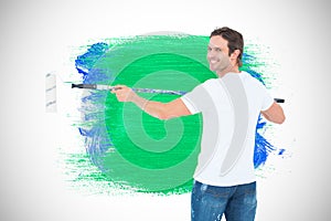 Composite image of happy man using paint roller
