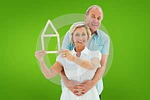 Composite image of happy older couple holding house shape