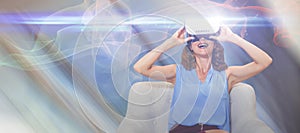 Composite image of happy woman using virtual reality glasses while sitting on sofa