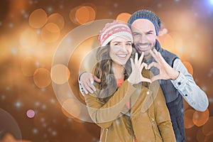 Composite image of happy young couple making heart shape with hands