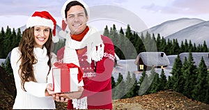 Composite image of happy young couple in santa hats with christmas present, copy space