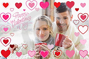 Composite image of loving couple in winter clothing with coffee cups against window