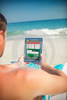 Composite image of man using digital tablet on deck chair at the beach