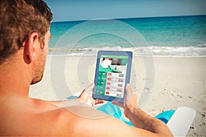 Composite image of man using digital tablet on deck chair at the beach