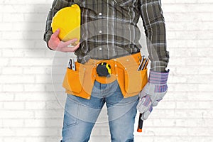 Composite image of manual worker wearing tool belt while holding gloves and helmet