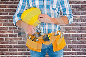 Composite image of manual worker wearing tool belt while holding hammer and helmet