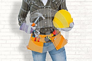 Composite image of manual worker wearing tool belt while holding hammer and helmet