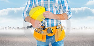 Composite image of manual worker wearing tool belt while holding hammer and helmet