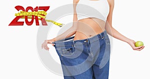 Composite image of mid section of slim woman wearing too big jeans holding an apple