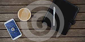 Composite image of mobile phone, coffee, pen and organizer on wooden plank