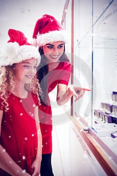 Composite image of mother and daughter in christmas attire looking at jewelry display