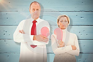 Composite image of older couple standing holding broken pink heart