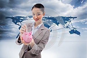 Composite image of portrait of a businesswoman putting a bank note in a piggy bank