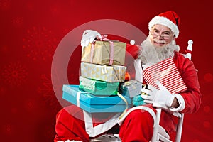 Composite image of portrait of cheerful santa claus holding christmas presents on chair