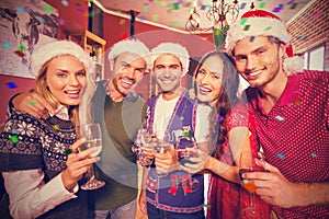 Composite image of portrait of friends wearing christmas hats with champagne flute