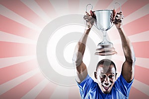 Composite image of portrait of happy athlete cheering while holding trophy