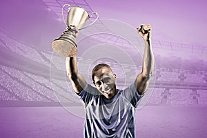 Composite image of portrait of happy sportsman cheering while holding trophy