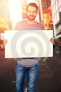 Composite image of portrait of smiling young man holding cardboard against white background