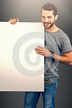 Composite image of portrait of smiling young man holding placard against white background