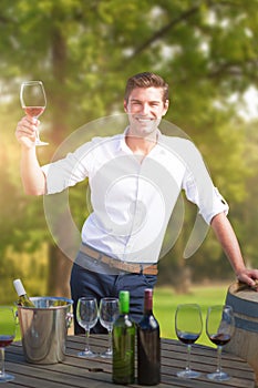 Composite image of portrait of smiling young man holding red wine glass by barrels