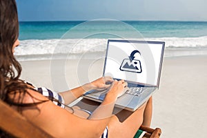 Composite image of pretty brunette using laptop on deck chair