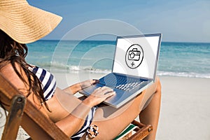 Composite image of pretty brunette using laptop on deck chair