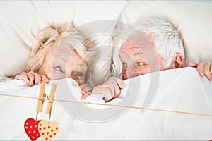 Composite image of red hanging hearts and senior couple relaxing on bed