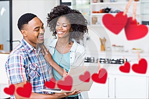 Composite image of red hanging hearts and smiling couple using laptop