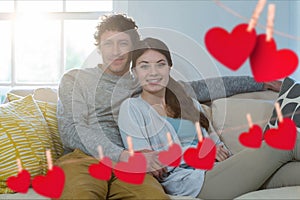 Composite image of red heart and couple embracing on sofa