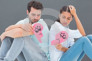 Composite image of sad couple sitting holding two halves of broken heart