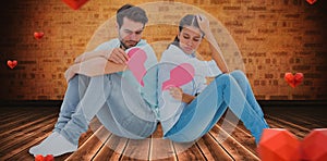 Composite image of sad couple sitting holding two halves of broken heart