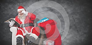 Composite image of santa reading bible with sack of christmas present beside him