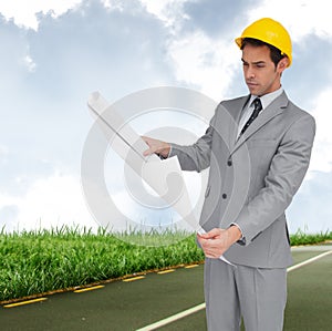 Composite image of serious architect with hard hat looking at plans