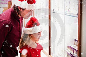 Composite image of side view of father and daughter in christmas attire looking at jewelry display