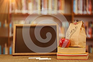 Composite image of slate with chalks by lunch bag and books on wooden table